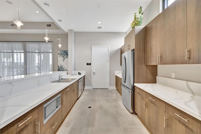 kitchen with appliances with stainless steel finishes, light tile patterned floors, light stone counters, and decorative light fixtures