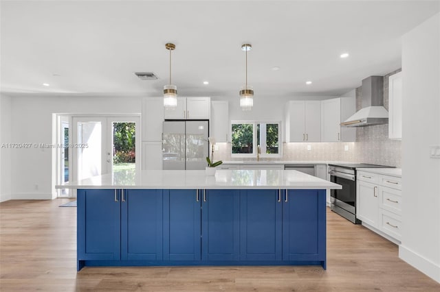 kitchen featuring stainless steel appliances, a center island, white cabinets, and wall chimney range hood