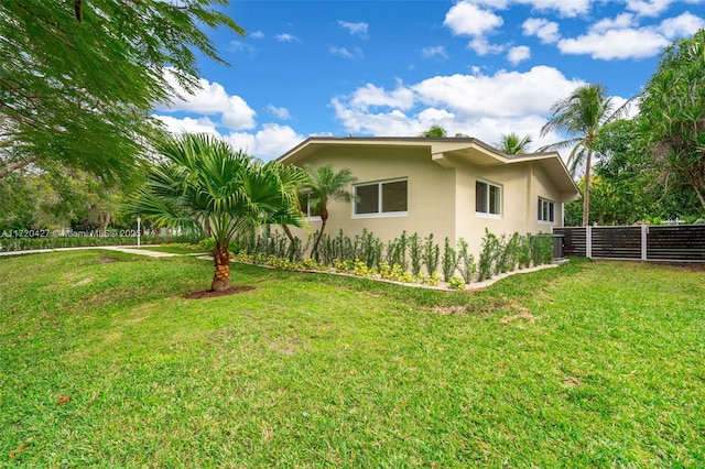 view of property exterior featuring a lawn, fence, and stucco siding