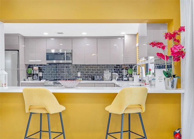 kitchen featuring a kitchen breakfast bar, gray cabinets, tasteful backsplash, and appliances with stainless steel finishes