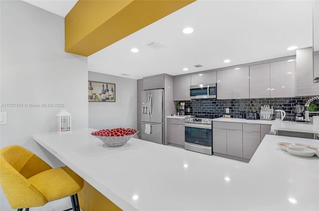 kitchen featuring kitchen peninsula, stainless steel appliances, a breakfast bar area, and gray cabinetry