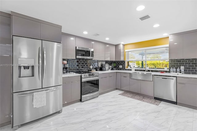 kitchen featuring gray cabinets, decorative backsplash, sink, and appliances with stainless steel finishes