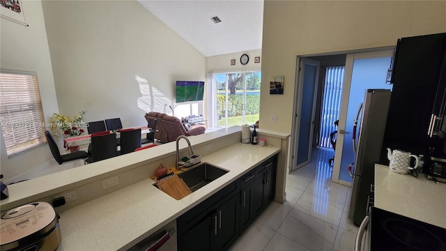 kitchen featuring stainless steel fridge, a textured ceiling, sink, light tile patterned floors, and lofted ceiling