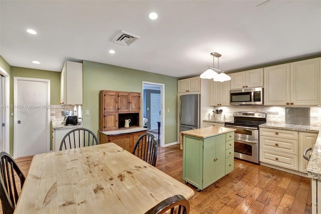 kitchen with light stone countertops, backsplash, stainless steel appliances, decorative light fixtures, and a kitchen island