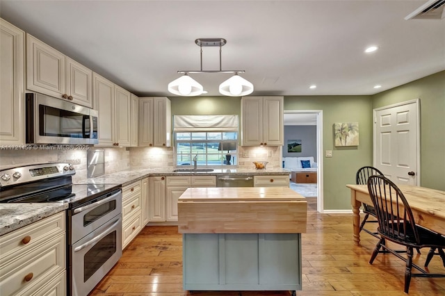 kitchen featuring stainless steel appliances, light stone counters, backsplash, decorative light fixtures, and a kitchen island