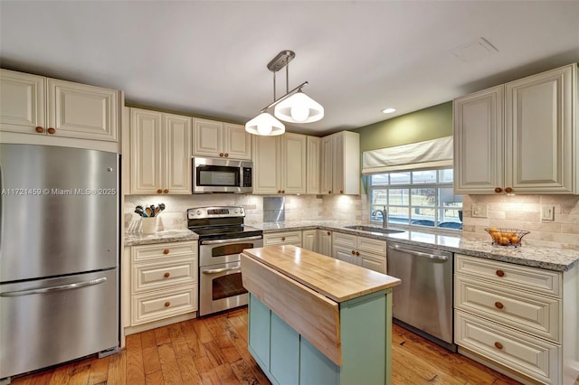 kitchen with sink, light hardwood / wood-style flooring, appliances with stainless steel finishes, decorative light fixtures, and light stone counters