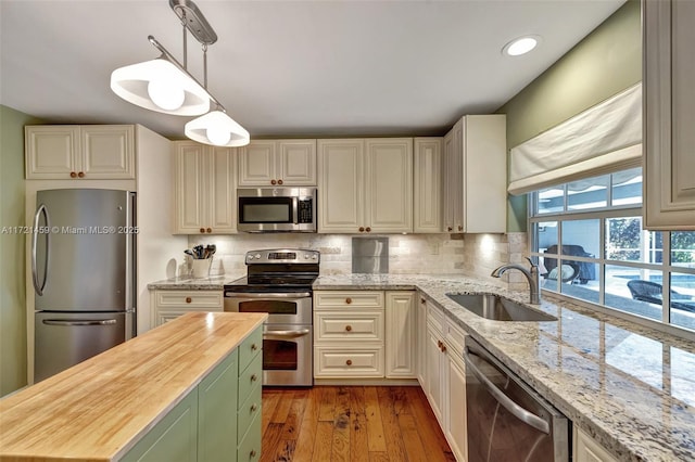 kitchen with pendant lighting, sink, light hardwood / wood-style flooring, butcher block counters, and stainless steel appliances