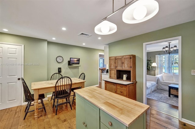 kitchen with an inviting chandelier, green cabinets, decorative light fixtures, a kitchen island, and wood-type flooring