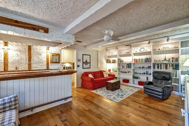 living area featuring a textured ceiling, light hardwood / wood-style flooring, ceiling fan, and wood walls