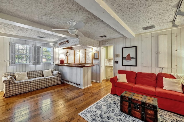 living room featuring beam ceiling, ceiling fan, wooden walls, and hardwood / wood-style flooring