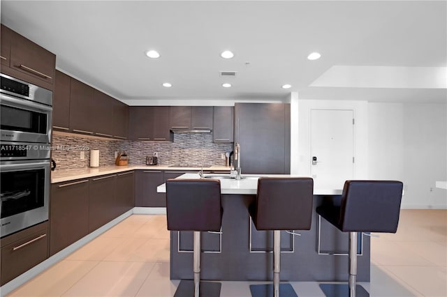 kitchen with visible vents, decorative backsplash, light countertops, stainless steel double oven, and a kitchen bar