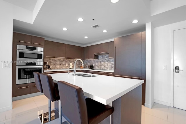 kitchen with light countertops, a kitchen bar, a sink, and a kitchen island with sink