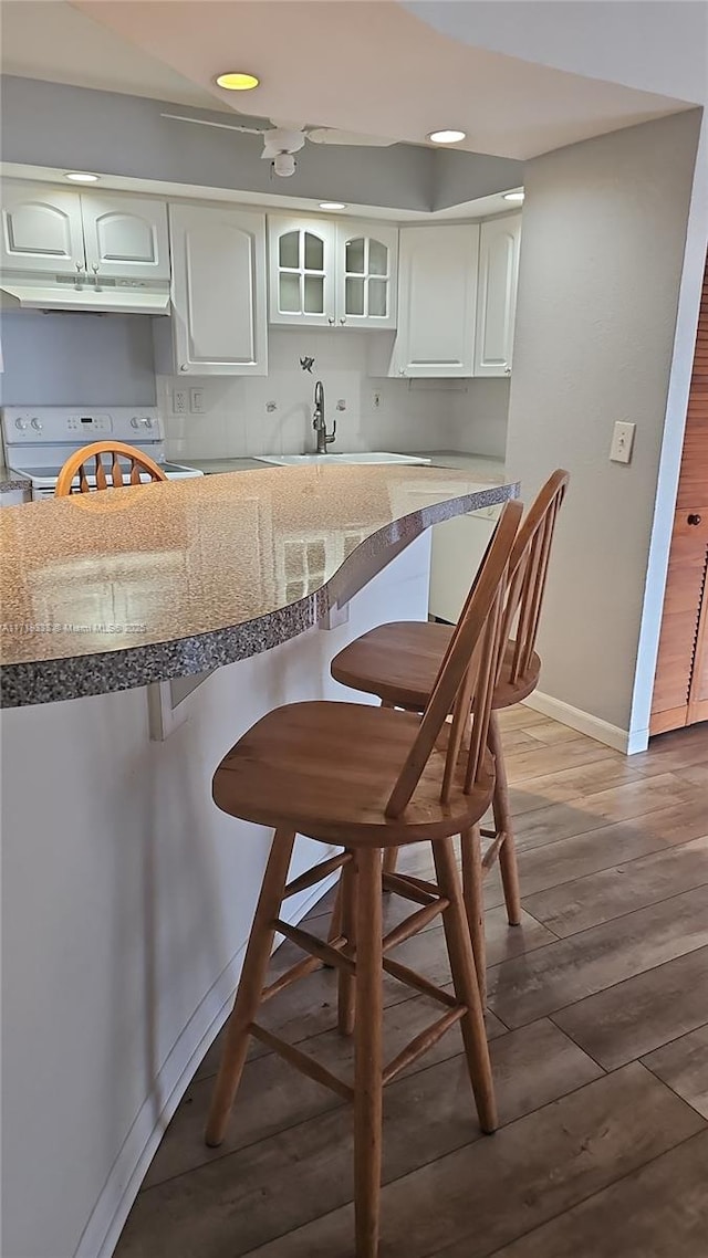 kitchen with white electric range, sink, white cabinets, a kitchen bar, and hardwood / wood-style flooring