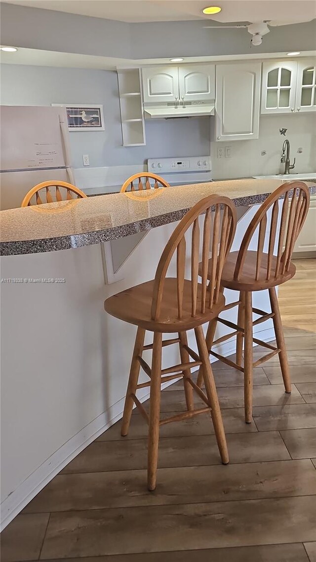 kitchen with white appliances, wood-type flooring, a kitchen breakfast bar, and white cabinets