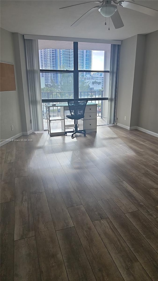 empty room featuring expansive windows, wood-type flooring, and ceiling fan