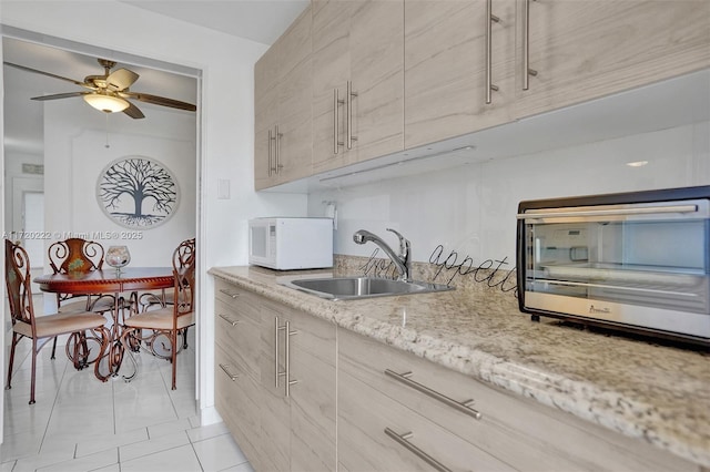 kitchen featuring light stone counters, sink, light tile patterned flooring, and ceiling fan