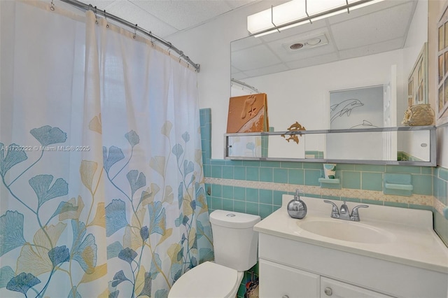 bathroom with a drop ceiling, toilet, tile walls, and vanity