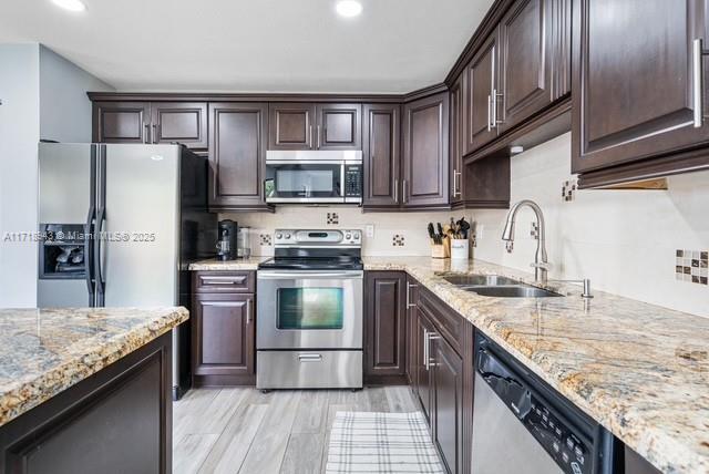 kitchen with light stone counters, light hardwood / wood-style floors, sink, and stainless steel appliances