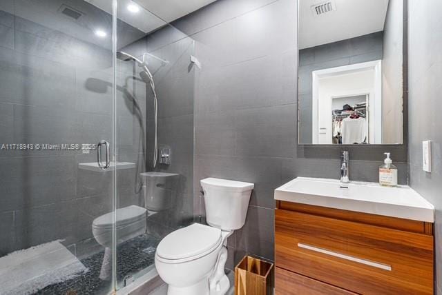 bathroom with a shower with door, vanity, tile walls, and toilet