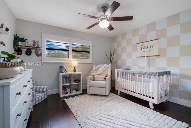 bedroom featuring ceiling fan, a crib, and dark wood-type flooring