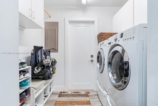 laundry room featuring washing machine and dryer, light hardwood / wood-style flooring, cabinets, and electric panel