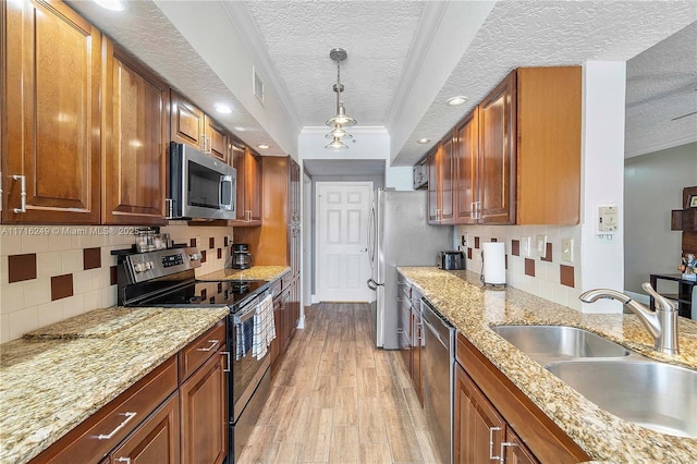 kitchen with appliances with stainless steel finishes, light stone counters, sink, pendant lighting, and light hardwood / wood-style flooring