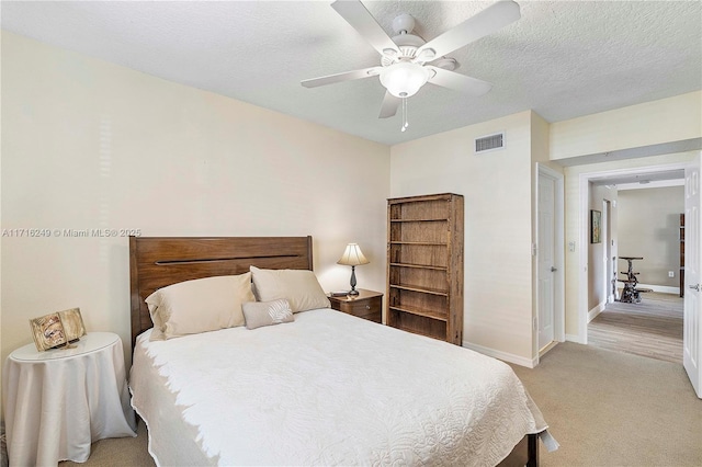 bedroom featuring a textured ceiling, light colored carpet, and ceiling fan