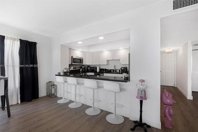 kitchen featuring kitchen peninsula, appliances with stainless steel finishes, a breakfast bar, dark hardwood / wood-style floors, and white cabinetry