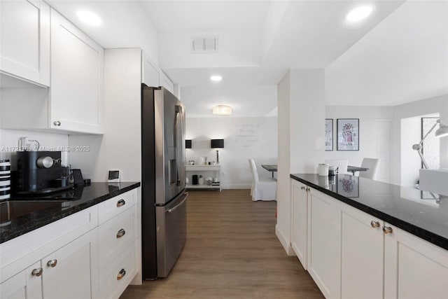 kitchen with stainless steel refrigerator with ice dispenser, hardwood / wood-style flooring, white cabinetry, and dark stone countertops