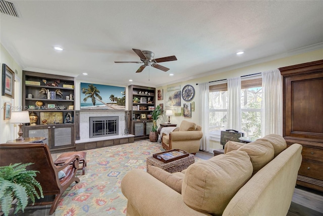 living room with a tiled fireplace, hardwood / wood-style floors, crown molding, built in features, and ceiling fan