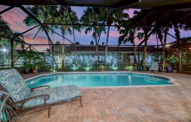 pool at dusk featuring a lanai and a patio