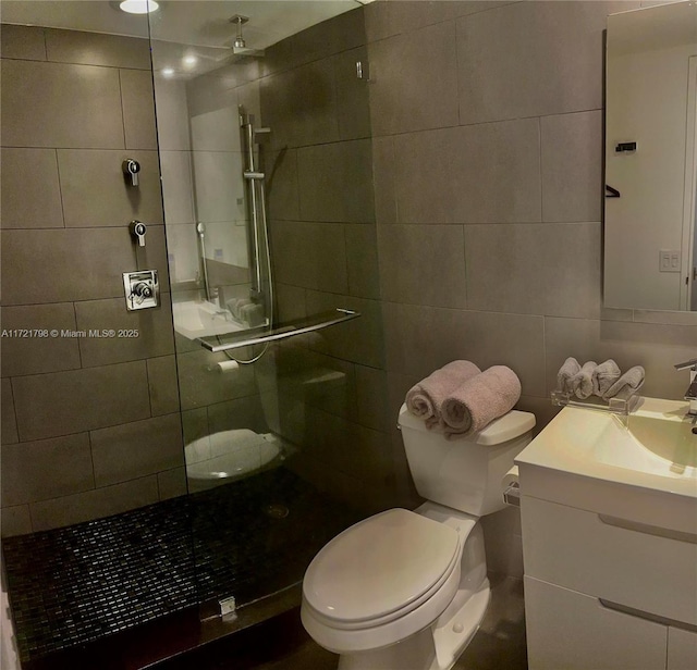 bathroom featuring vanity, toilet, a shower with door, and tile walls