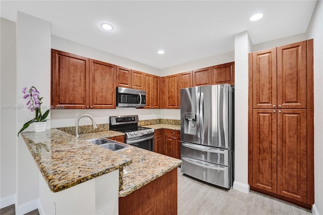 kitchen with sink, light stone counters, light hardwood / wood-style flooring, kitchen peninsula, and appliances with stainless steel finishes