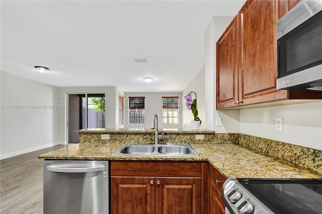 kitchen featuring kitchen peninsula, appliances with stainless steel finishes, light stone counters, and sink