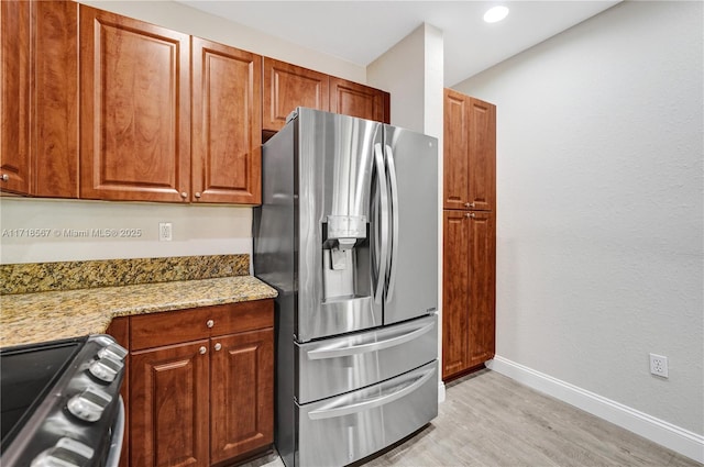 kitchen with stainless steel fridge with ice dispenser, stove, light stone counters, and light hardwood / wood-style floors