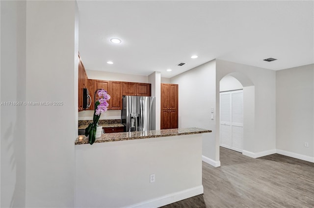 kitchen featuring hardwood / wood-style flooring, kitchen peninsula, light stone countertops, and stainless steel appliances