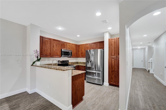 kitchen with kitchen peninsula, appliances with stainless steel finishes, light stone countertops, sink, and light hardwood / wood-style floors