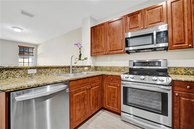 kitchen with kitchen peninsula, light stone countertops, sink, and appliances with stainless steel finishes