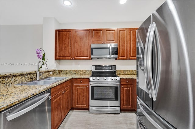 kitchen featuring light stone countertops, light wood-type flooring, stainless steel appliances, and sink