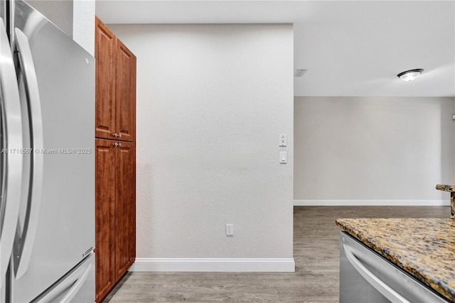 kitchen with light hardwood / wood-style floors, light stone countertops, and appliances with stainless steel finishes