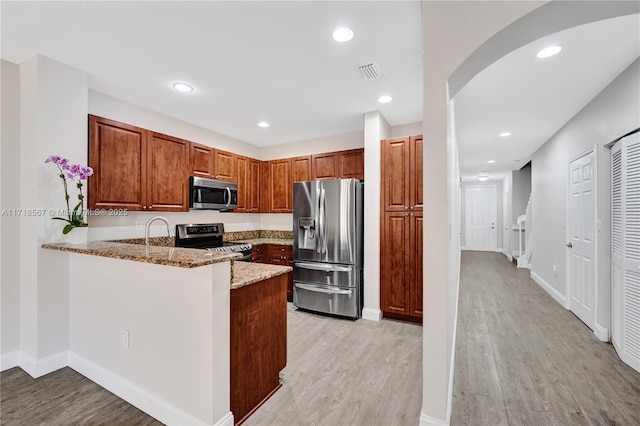 kitchen with kitchen peninsula, light stone counters, light wood-type flooring, and appliances with stainless steel finishes