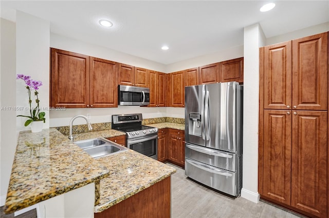 kitchen featuring sink, light hardwood / wood-style floors, light stone counters, kitchen peninsula, and stainless steel appliances