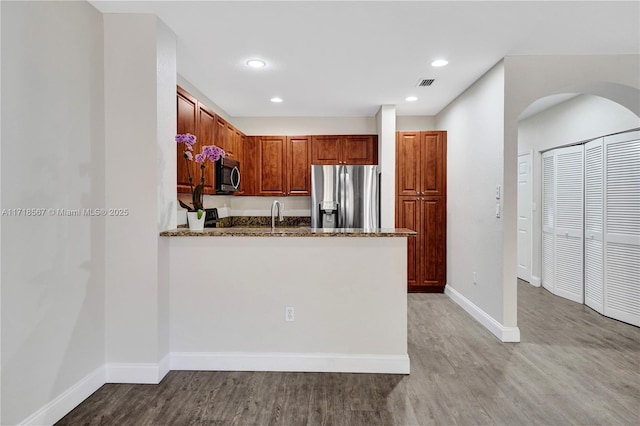 kitchen featuring stone counters, light hardwood / wood-style floors, kitchen peninsula, and appliances with stainless steel finishes