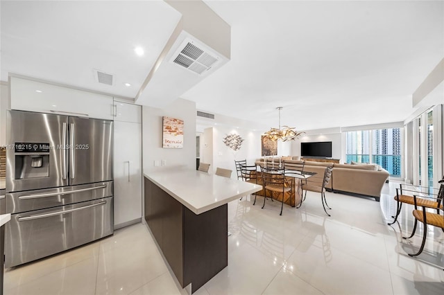 kitchen featuring white cabinets, stainless steel refrigerator with ice dispenser, light tile patterned floors, decorative light fixtures, and kitchen peninsula