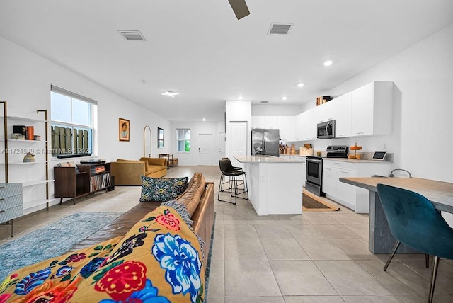 kitchen with a kitchen breakfast bar, light tile patterned floors, appliances with stainless steel finishes, a kitchen island, and white cabinetry