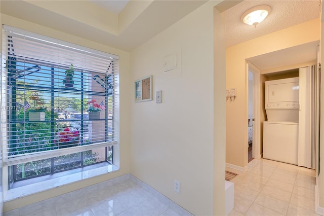 hall featuring stacked washer and dryer, light tile patterned floors, and a textured ceiling