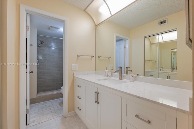 bathroom with a tile shower, tile patterned floors, a textured ceiling, toilet, and vanity