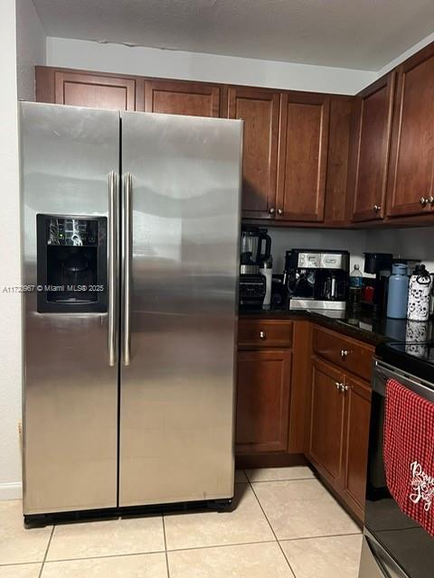 kitchen with stainless steel fridge with ice dispenser, light tile patterned floors, and black range oven