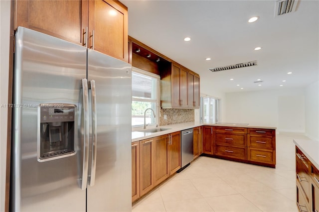 kitchen with sink, kitchen peninsula, decorative backsplash, light tile patterned floors, and appliances with stainless steel finishes