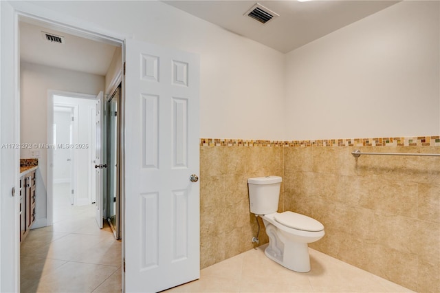 bathroom featuring tile patterned flooring, vanity, toilet, and tile walls